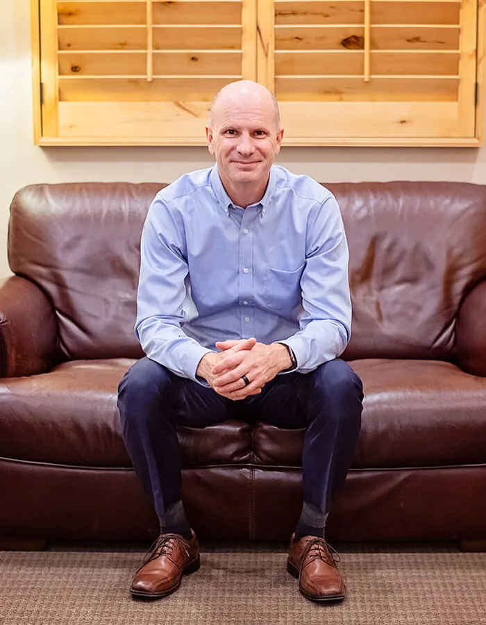 Dr. Ryan Speirs sitting on a brown leather sofa